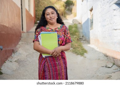 Hispanic mom with notebooks outside school in rural area - Mayan adult woman ready to go to study - Latina teacher in town - Shutterstock ID 2118679880