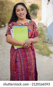 Hispanic mom with notebooks outside school in rural area - Mayan adult woman ready to go to study - Latina teacher in town - Shutterstock ID 2120166593