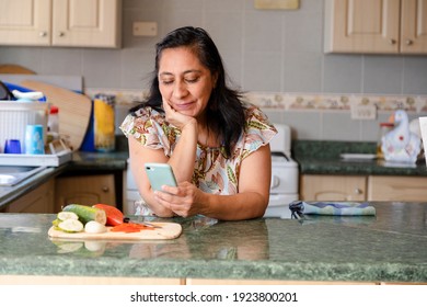 Hispanic Mom Searching Recipes On Her Phone-woman Preparing Healthy And Organic Salad While Checking Her Cell Phone-bored Housewife While She Looks At Her Phone