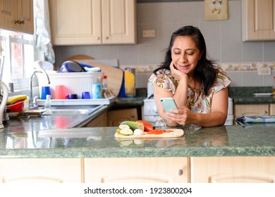 Hispanic Mom Searching Recipes On Her Phone-woman Preparing Healthy And Organic Salad While Checking Her Cell Phone-housewife Cooking While She Looks At A Phone