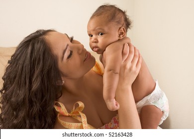 Hispanic Mom Sitting On Bed And Holding Her Biracial Mix Of Hispanic And African American Infant Son (baby Is 7 Weeks Old)