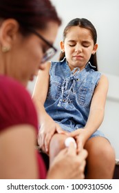 Hispanic Mom Treating Wound On Daughter's Injured Knee. Family Life At Home With Latina Woman Helping And Taking Care Of Sick Little Girl.