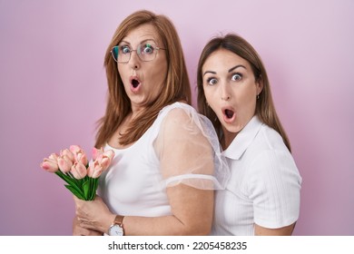 Hispanic Mother And Daughter Holding Pink Tulips Bouquet Scared And Amazed With Open Mouth For Surprise, Disbelief Face 