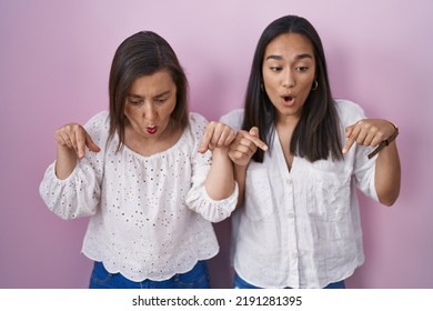 Hispanic Mother And Daughter Together Pointing Down With Fingers Showing Advertisement, Surprised Face And Open Mouth 