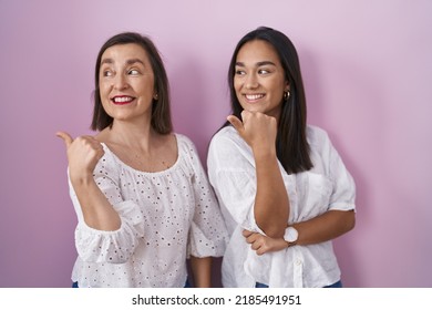 Hispanic Mother And Daughter Together Smiling With Happy Face Looking And Pointing To The Side With Thumb Up. 