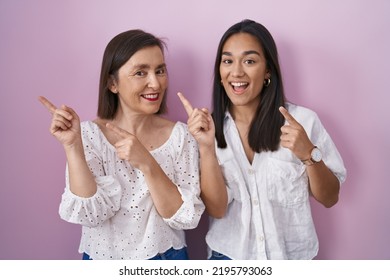 Hispanic Mother And Daughter Together Smiling And Looking At The Camera Pointing With Two Hands And Fingers To The Side. 