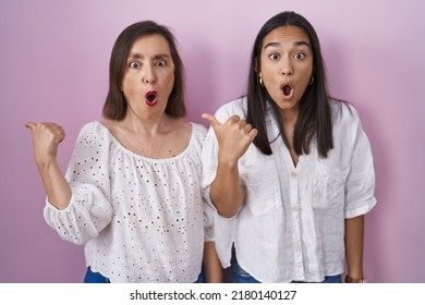 Hispanic Mother And Daughter Together Surprised Pointing With Hand Finger To The Side, Open Mouth Amazed Expression. 