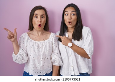 Hispanic Mother And Daughter Together Surprised Pointing With Finger To The Side, Open Mouth Amazed Expression. 