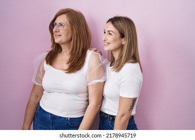 Hispanic Mother And Daughter Wearing Casual White T Shirt Over Pink Background Looking Away To Side With Smile On Face, Natural Expression. Laughing Confident. 