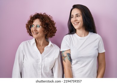 Hispanic Mother And Daughter Wearing Casual White T Shirt Over Pink Background Looking Away To Side With Smile On Face, Natural Expression. Laughing Confident. 