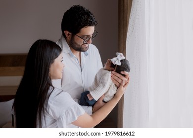 Hispanic Mother And Father Smiling While Holding Their Newborn Baby In Their Arms - Happy Young Latino Parents With Their Newborn Baby