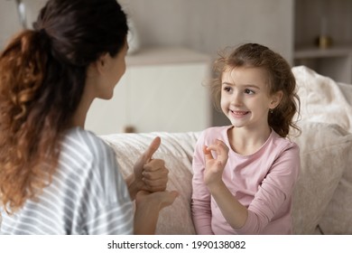 Hispanic mother and small ethnic daughter talk communicate using hand gestures. Cute little teen biracial disabled kid child practice speak with sign language with mom or coach. Nonverbal concept. - Powered by Shutterstock