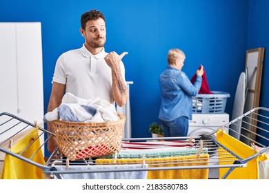 Hispanic Mother And Son Hanging Clothes At Clothesline Pointing Thumb Up To The Side Smiling Happy With Open Mouth 