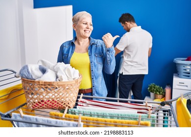 Hispanic Mother And Son Hanging Clothes At Clothesline Pointing Thumb Up To The Side Smiling Happy With Open Mouth 