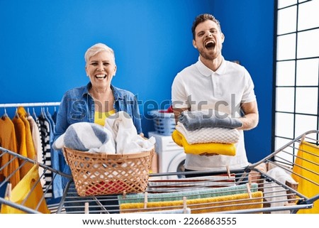 Hispanic mother and son hanging clothes at clothesline smiling and laughing hard out loud because funny crazy joke. 