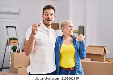 Hispanic Mother And Son Holding Keys Of New Home Pointing Thumb Up To The Side Smiling Happy With Open Mouth 