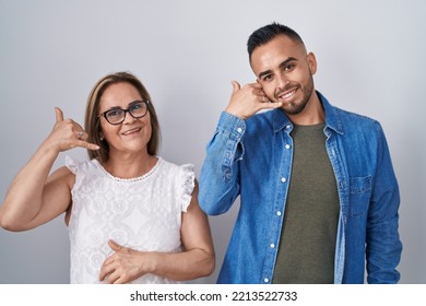 Hispanic Mother And Son Standing Together Smiling Doing Phone Gesture With Hand And Fingers Like Talking On The Telephone. Communicating Concepts. 