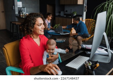 Hispanic mother using computer to work at home while she takes care of his baby son in Mexico Latin America, home office concept