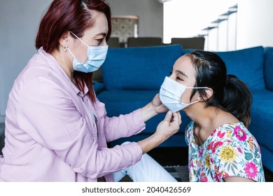 Hispanic Mother Wearing Face Mask On Her Daughter With Cerebral Palsy At Home In Latin America In Disability Concept During Covid Coronavirus Pandemic