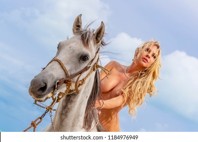 A hispanic nude brunette model rides a horse on a Caribbean beach