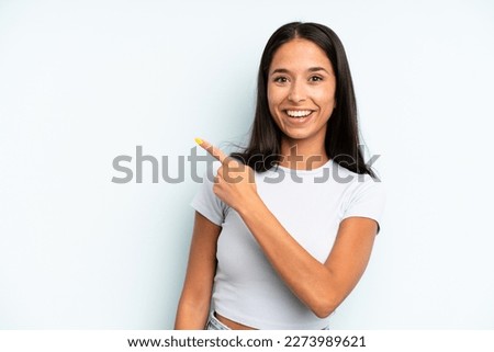 hispanic pretty woman looking excited and surprised pointing to the side and upwards to copy space