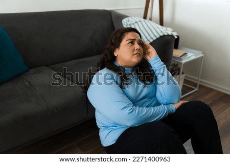Hispanic sad woman looking tired and depressed while sitting in the living room having mental health problems