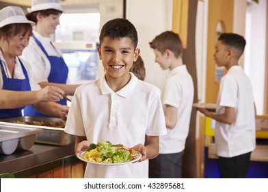 Hispanic Schoolboy Holds A Plate Of Food In School Cafeteria