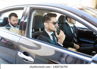 Hispanic security person using radio transceiver while transporting businessman in car - Powered by Shutterstock