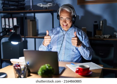 Hispanic Senior Man Wearing Call Center Agent Headset At Night Success Sign Doing Positive Gesture With Hand, Thumbs Up Smiling And Happy. Cheerful Expression And Winner Gesture. 