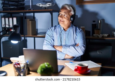 Hispanic Senior Man Wearing Call Center Agent Headset At Night Smiling Looking To The Side And Staring Away Thinking. 