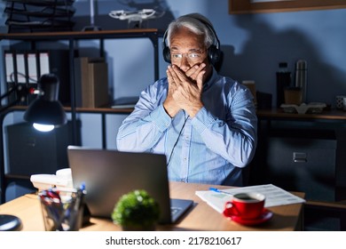 Hispanic Senior Man Wearing Call Center Agent Headset At Night Shocked Covering Mouth With Hands For Mistake. Secret Concept. 