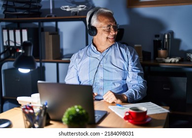 Hispanic Senior Man Wearing Call Center Agent Headset At Night Looking Away To Side With Smile On Face, Natural Expression. Laughing Confident. 