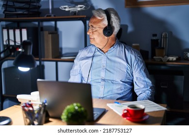 Hispanic Senior Man Wearing Call Center Agent Headset At Night Looking To Side, Relax Profile Pose With Natural Face With Confident Smile. 