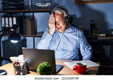 Hispanic Senior Man Wearing Call Center Agent Headset At Night Covering One Eye With Hand, Confident Smile On Face And Surprise Emotion. 