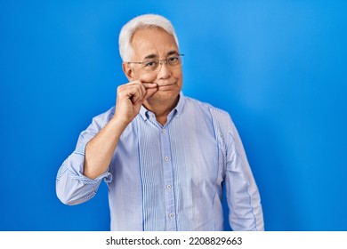 Hispanic Senior Man Wearing Glasses Mouth And Lips Shut As Zip With Fingers. Secret And Silent, Taboo Talking 