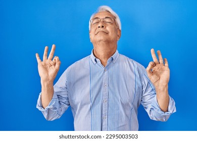 Hispanic senior man wearing glasses relaxed and smiling with eyes closed doing meditation gesture with fingers. yoga concept.  - Powered by Shutterstock