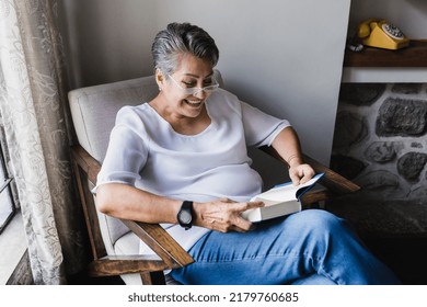 hispanic senior woman reading book and sitting on sofa at home in Mexico Latin America - Powered by Shutterstock