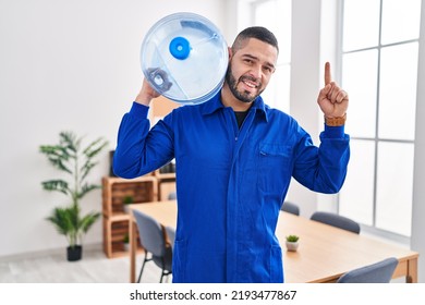 Hispanic Service Man Holding A Gallon Bottle Of Water For Delivery Surprised With An Idea Or Question Pointing Finger With Happy Face, Number One 