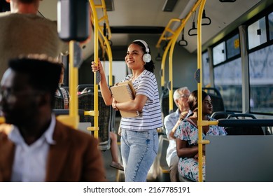 Hispanic student with earphones traveling in public transport. Smiling girl is standing at aisle while commuting by bus. - Powered by Shutterstock