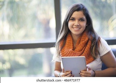 Hispanic Student smiling, looking up from tablet at library in university wearing her winter scarf
