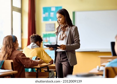 Hispanic teacher using touchpad while communicating with her student during a class at primary school.