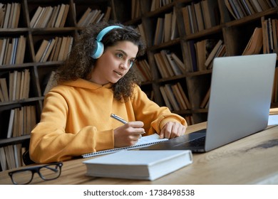 Hispanic teen girl, latin young woman school college student wear headphones learn watching online webinar webcast class looking at laptop elearning making notes or video calling remote teacher.