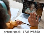 Hispanic teen girl school college student distance learning waving hand studying with online teacher on laptop screen. Elearning zoom video call, videoconference class with tutor. Over shoulder view.