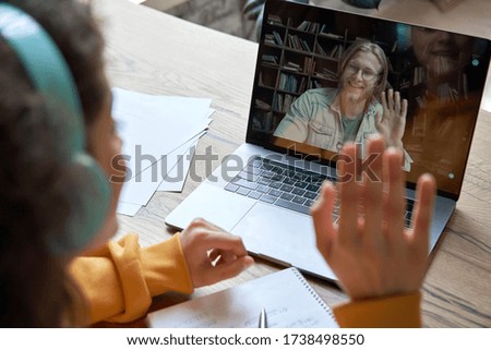 Hispanic teen girl school college student distance learning waving hand studying with online teacher on laptop screen. Elearning zoom video call, videoconference class with tutor. Over shoulder view.