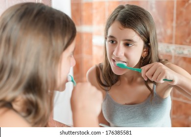 Hispanic Teenage Girl Brushing Her Teeth In Front Of A Mirror