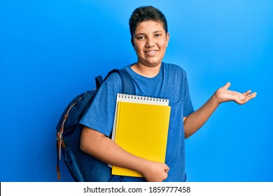 Hispanic teenager boy wearing student backpack and holding books doing ok sign with fingers, smiling friendly gesturing excellent symbol 