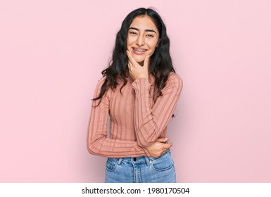 Hispanic Teenager Girl With Dental Braces Wearing Casual Clothes Looking Confident At The Camera Smiling With Crossed Arms And Hand Raised On Chin. Thinking Positive. 