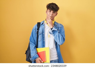 Hispanic teenager wearing student backpack and holding books with hand on chin thinking about question, pensive expression. smiling with thoughtful face. doubt concept.  - Shutterstock ID 2348020339
