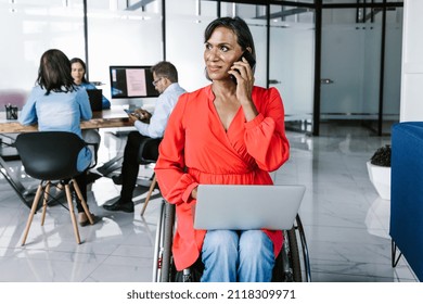 Hispanic Transgender Businesswoman In Wheelchair Calling On Cell Phone With Laptop On Her Legs At Work In Mexico City