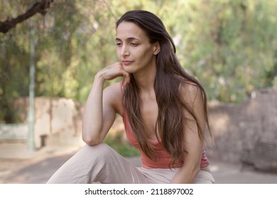 Hispanic Woman, 30 Years Old, Long Straight Hair. Sitting In A Park.